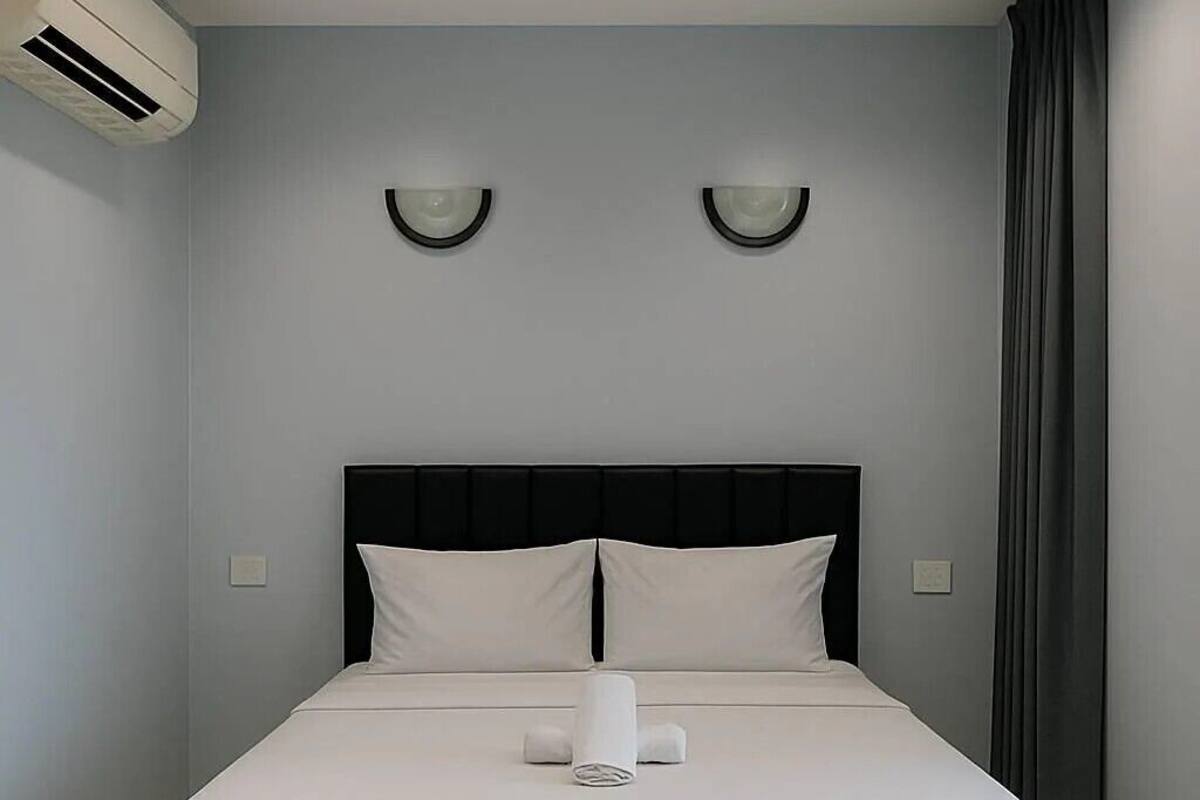 A modern hotel room with a large bed, a black headboard, and two wall-mounted lights.