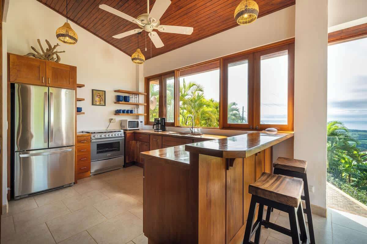 Una cucina con un'isola grande, elettrodomestici in acciaio inossidabile, mobili in legno e vista all'esterno.