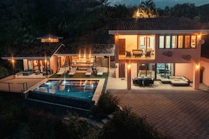 A modern house with a swimming pool, outdoor seating, and a well-lit interior. - 5BR/6BA Luxury Jungle Villa w/ Breathtaking Views! (Playa Hermosa)