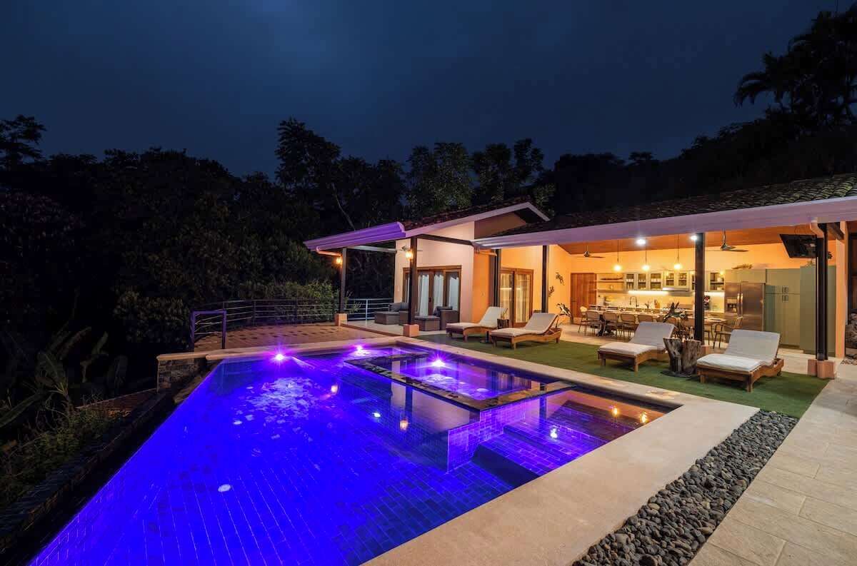 A modern house with a swimming pool, outdoor seating, and a well-lit interior.