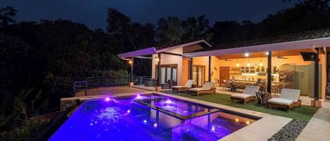 A modern house with a swimming pool, outdoor seating, and a well-lit interior.