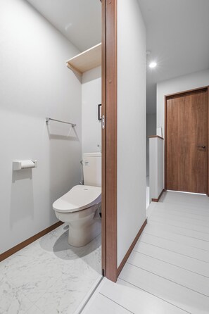 A modern bathroom with a toilet, a towel rack, and a wooden door.