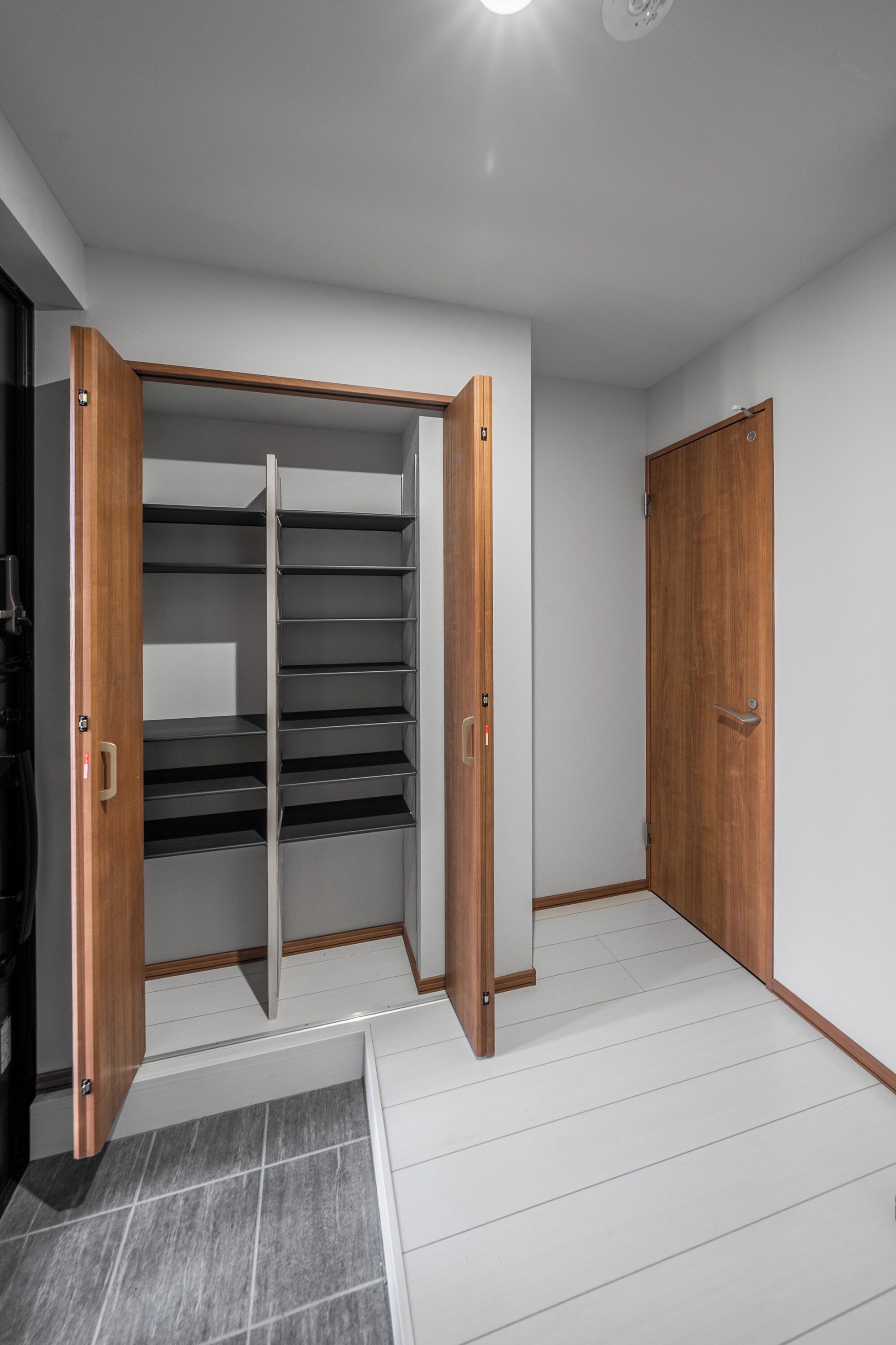 A room with a wooden wardrobe, a white door, and a tiled floor.