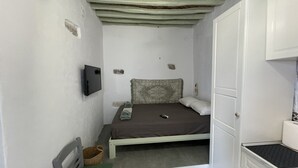 Una habitación pequeña con una cama individual, cabecera de madera, televisor montado en la pared y un ventanal.