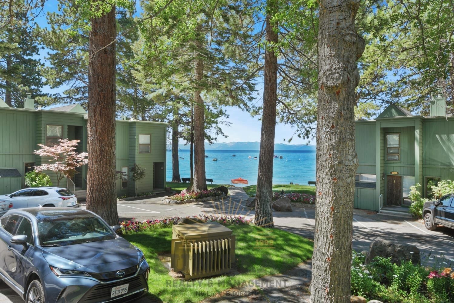 A row of green cabins with a view of the lake and mountains in the background.