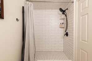 A shower with white tiled walls, a showerhead, and a small shelf with toiletries. - Charming Snowblaze 107 in Historic Park City For 6 People (Park City)