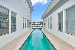 Un espace piscine moderne avec une eau d’un bleu limpide, de grandes fenêtres et une vue sur les palmiers.