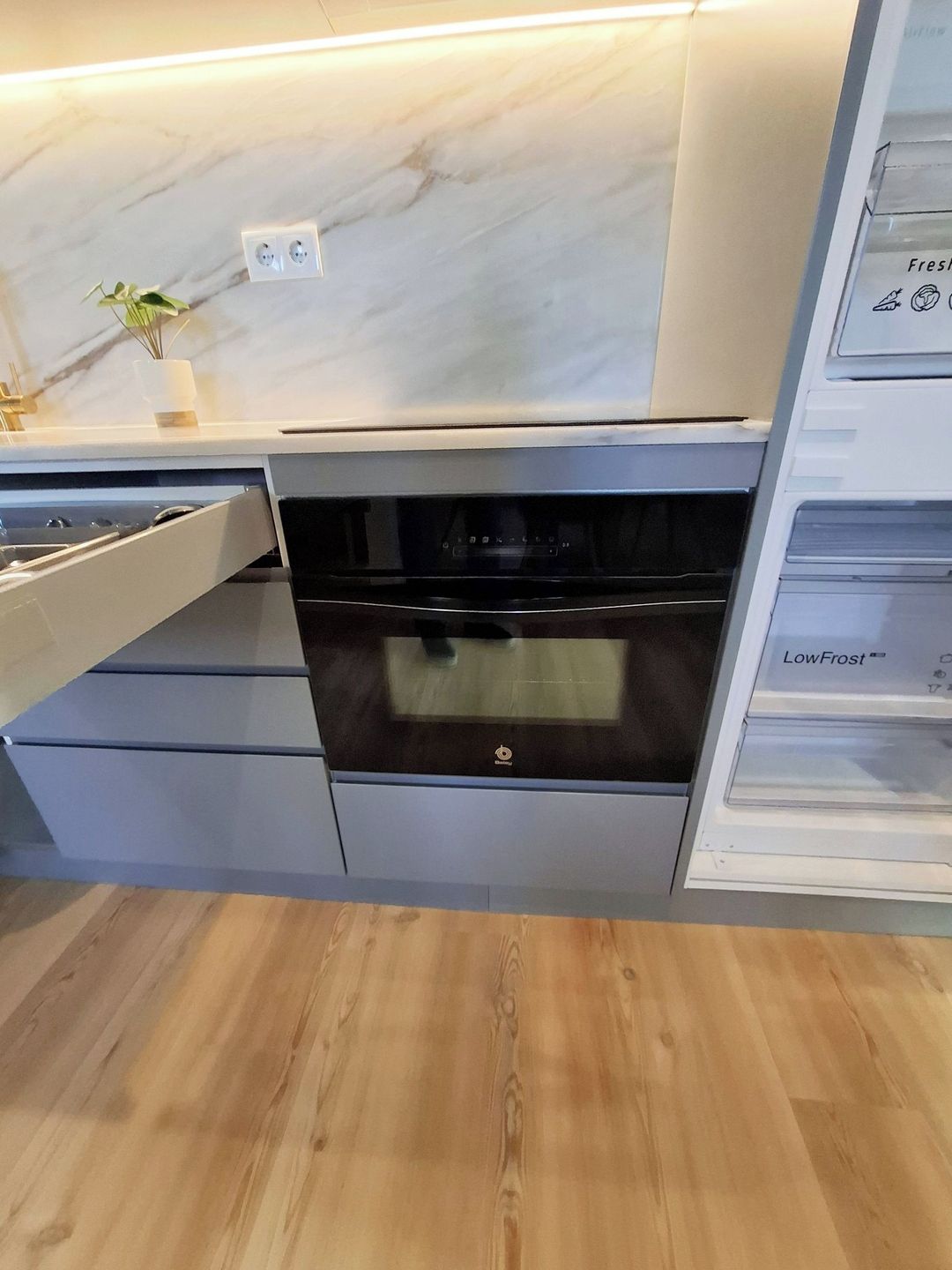 A modern kitchen with a built-in oven, a marble backsplash, and a wooden floor.