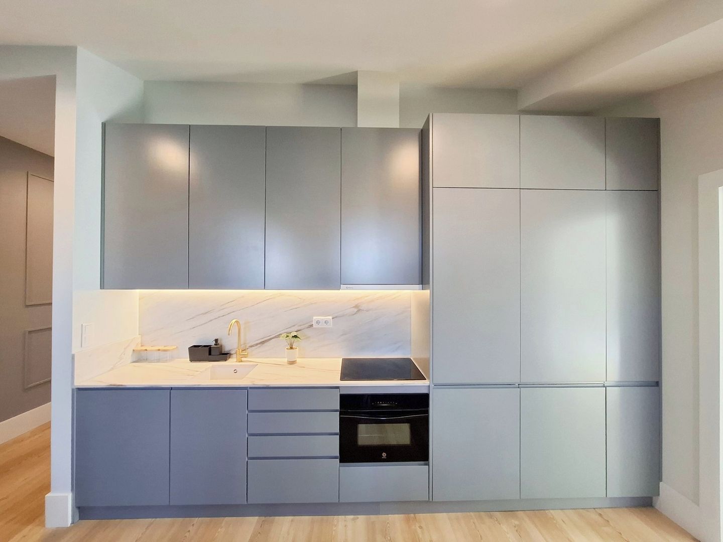 Une cuisine moderne avec des meubles gris, un plan de travail blanc et un four encastré.