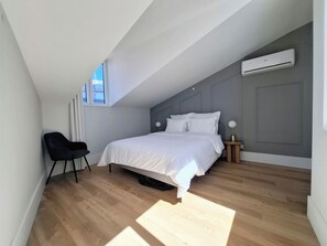 Ein Schlafzimmer mit Bett, Stuhl, Nachttisch, Klimaanlage und Fenster.