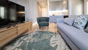 Un salon moderne avec un téléviseur à écran plat, un canapé gris, un fauteuil turquoise et un tapis à motifs.