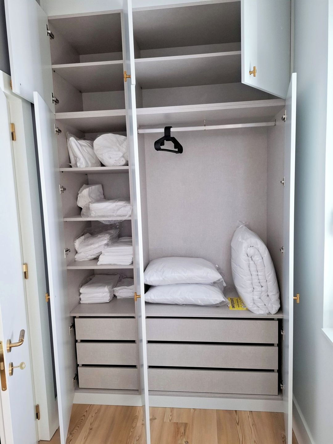 A walk-in closet with multiple shelves, drawers, and hanging space, featuring a minimalist design and light wood flooring.