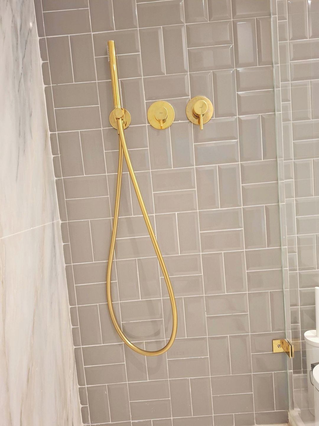 Ein Badezimmer mit Duschkabine, weißer Toilette und Wand mit Fischgrätmuster.