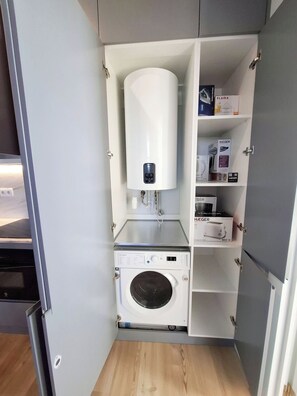 Ein kleiner Hauswirtschaftsraum mit einer Waschmaschine mit Frontlader, einer fest installierten Heizung und Regalen für Stauraum.
