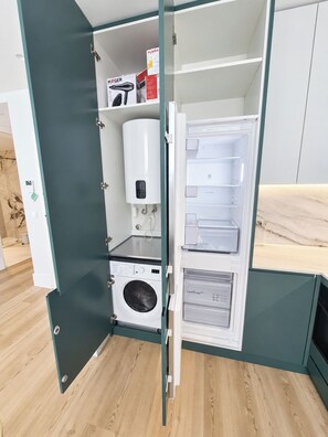 Eine kompakte Küche mit eingebauter Waschmaschine und Trockner, einem Kühlschrank und einem Durchlauferhitzer.