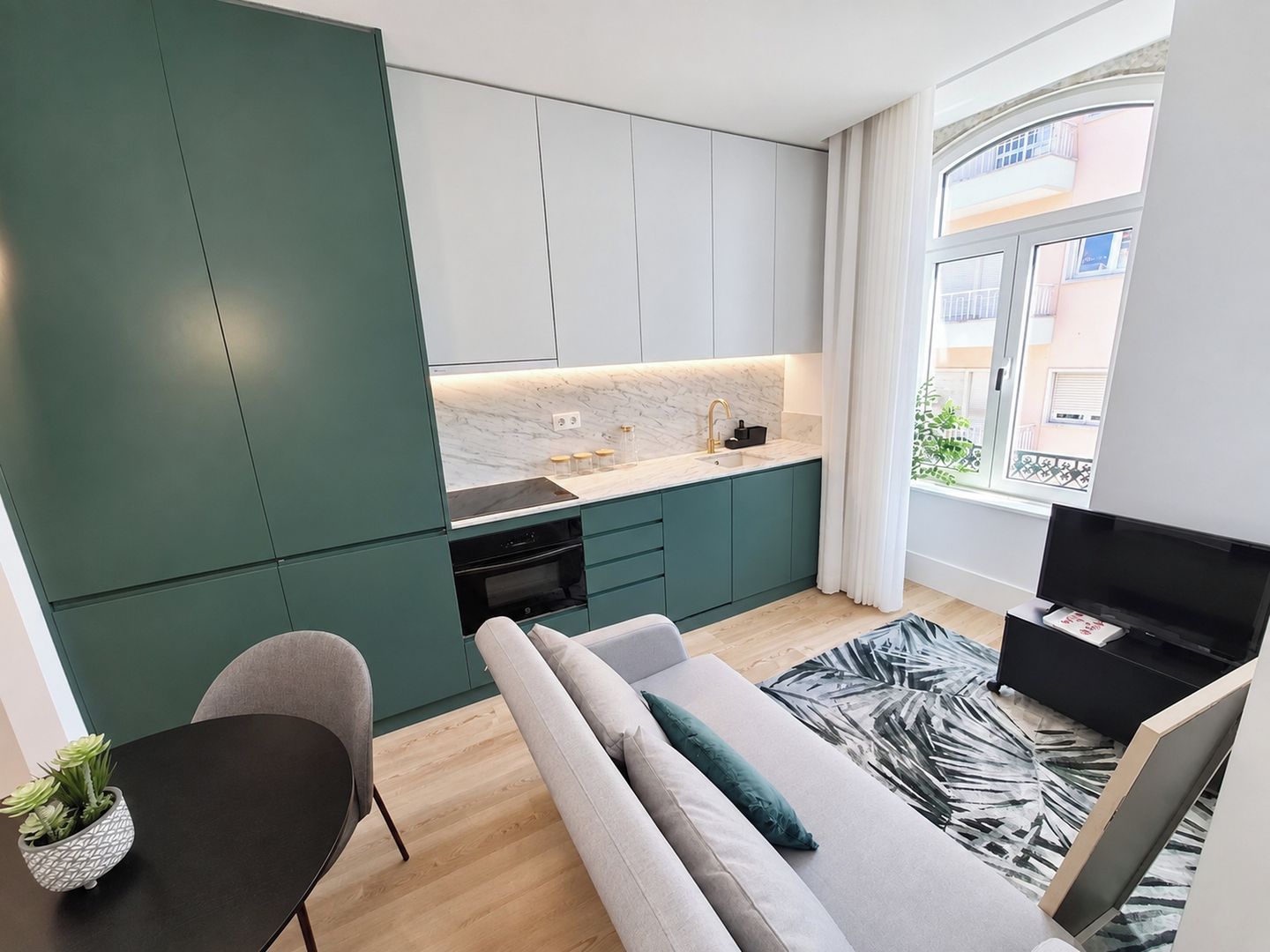 A compact living space with a kitchenette, a sofa, a TV, and a view of the outside.