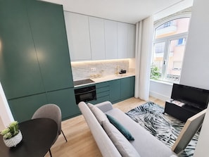 Um espaço de estar compacto com cozinha compacta, sofá, TV e vista para o exterior.