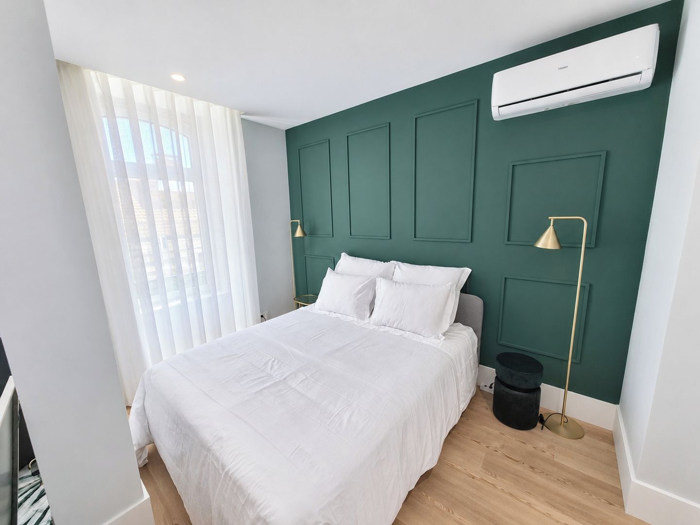 Un dormitorio moderno con cama, ventana con cortinas translúcidas, aire acondicionado de pared y una lámpara de pie.