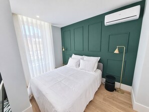 Ein modernes Schlafzimmer mit einem Bett, einem Fenster mit durchscheinenden Vorhängen, einer Wand-Klimaanlage und einer Stehlampe.