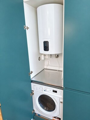 A compact, modern laundry room with a front-loading washing machine and a top-mounted water heater. - Studio 402 Lisbon • Elevator • AC • Wi-Fi (Lisbon)