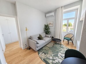 A modern living room with a sofa, a small table, a chair, a floor lamp, and a large window with a view. - Apartment 306 • Lisbon • 1 bedroom • Balcony • AC (Lisbon)