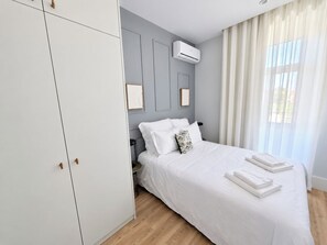 Une chambre à coucher avec un lit, des rideaux blancs, un appareil de climatisation et une armoire.