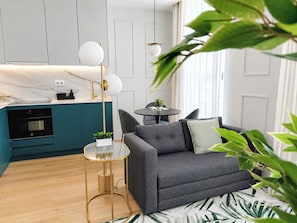A modern living room with a grey sofa, a small round table, and a kitchen area with teal cabinets and a marble countertop. - Studio 401 • Lisbon • Elevator • AC • Wi-Fi (Lisbon)