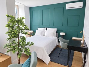 A modern bedroom with a teal accent wall, a bed with white linens, a desk with a lamp, and a potted plant. - Studio 401 • Lisbon • Elevator • AC • Wi-Fi (Lisbon)
