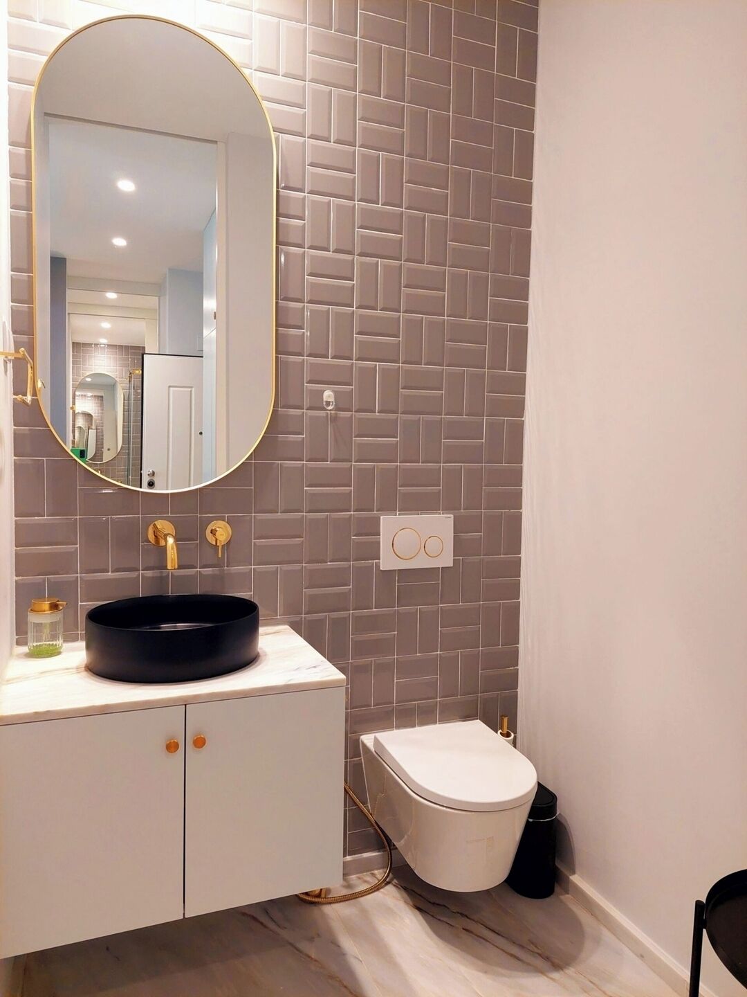 A bathroom with a round mirror, a black sink, a toilet, and a white cabinet.