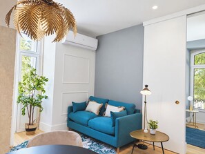 Ein modernes Wohnzimmer mit einem blauen Sofa, einem kleinen runden Tisch, einer Stehlampe und einem Blumentopf.