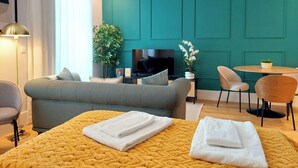 A modern hotel room with teal walls, a large bed with a yellow quilt, a grey sofa, a TV, a small table with chairs, and a potted plant. - Studio 205 Lisbon • Balcony • Elevator • AC • WiFi (Lisbon)