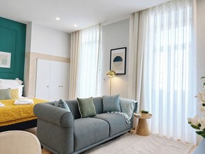 A modern bedroom with a grey sofa, a bed with a yellow bedspread, a bedside table with a lamp, and a window with sheer curtains. - Studio 205 Lisbon • Balcony • Elevator • AC • WiFi (Lisbon)