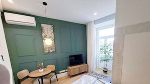 Una sala de estar moderna con una pared verde, una mesa redonda de comedor con sillas, un mueble para la televisión y una planta en maceta.