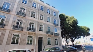 Un edificio de varios pisos con fachada decorada, balcones y coches estacionados en la calle.