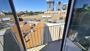 Vista desde un balcón con cielo despejado, que muestra edificios modernos, un estacionamiento y una vista distante del horizonte urbano.