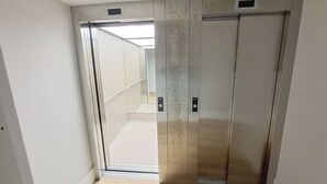 Een smalle gang met twee gesloten liftdeuren en een zichtbaar bedieningspaneel.