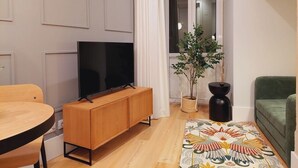 Een moderne woonkamer met een houten tv-meubel, een flatscreen televisie, een groene bank, een houten eettafel en een decoratief vloerkleed.