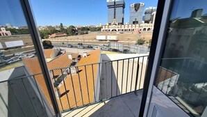 Vista desde un balcón con cielo despejado, que muestra edificios modernos, un estacionamiento y una vista distante del horizonte urbano.