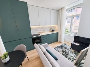 A modern apartment with a kitchen, a living area with a sofa and a TV, and a window with a view of buildings. - Studio 302 Lisbon • Balcony • Elevator • AC • WiFi (Lisbon)
