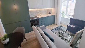 Een ruimtelijk ingerichte leefruimte met kitchenette, een bank, een klein tafeltje en een televisie.