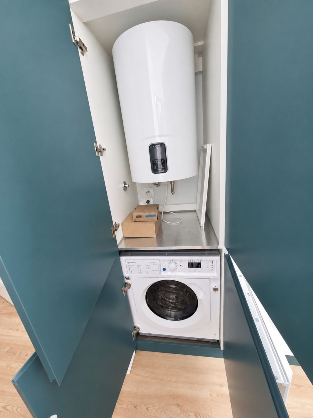 Une petite buanderie équipée d’un lave-linge blanc et d’un chauffe-eau cylindrique.