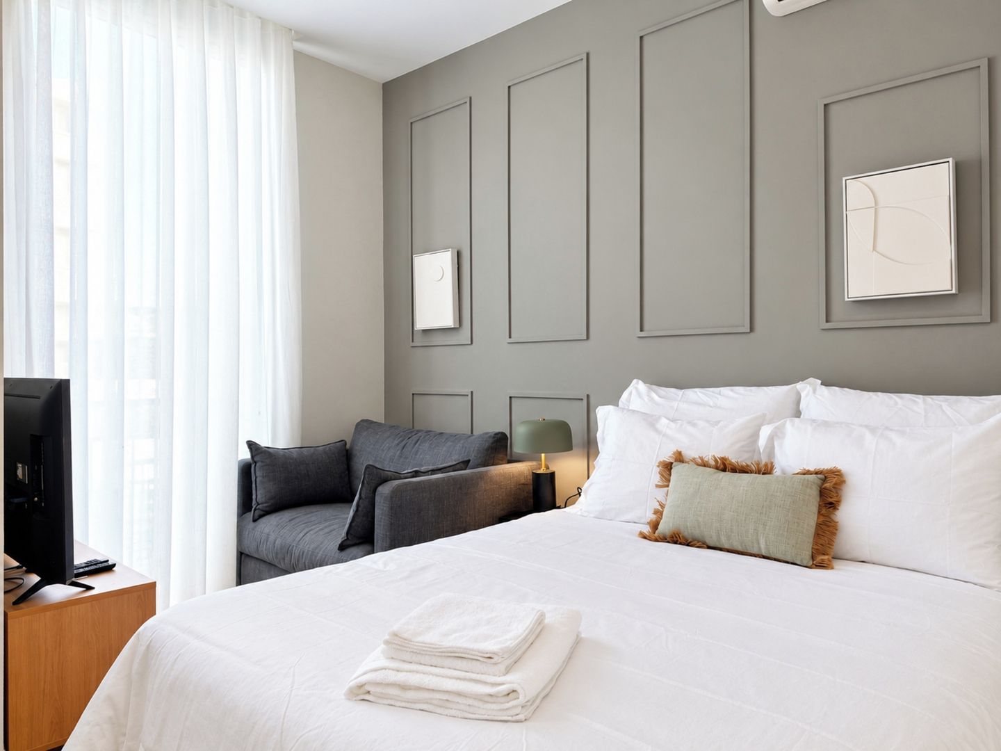 A hotel room with a bed, a desk, a television, and a window with curtains.