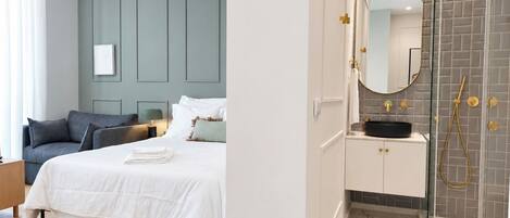 Een moderne hotelkamer met een bed, nachtkastje en een badkamer met douche en wastafel.