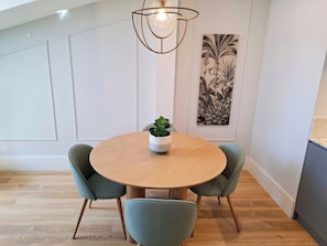 A dining area with a round wooden table, two upholstered chairs, a potted plant, and a wall-mounted light fixture. - Apartment 501 • Lisbon • 1 bedroom • Elevator • AC (Lisbon)