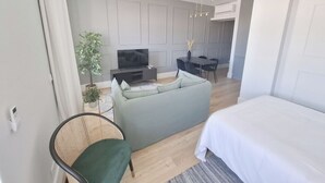 A modern living room with a sofa, TV, dining table, and chairs. - Studio Lisbon • Balcony • Elevator • AC • Parking (Lisbon)