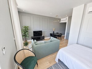 A modern bedroom with a bed, a green sofa, a television, and a dining area with chairs and a table. - Studio 305 Lisbon • Balcony • Elevator • AC • WiFi (Lisbon)