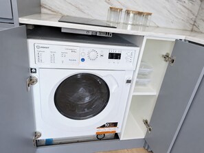 Una unidad compacta de lavadora y secadora con panel de control, ubicada en un armario de cocina con encimera de mármol.