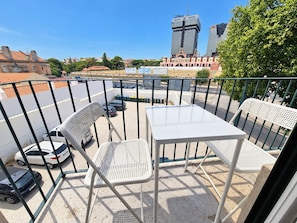 Ein Balkon mit zwei weißen Metallstühlen und einem Tisch, der auf einen Parkplatz und Gebäude blickt.