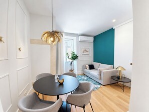 Een moderne woonkamer met een ronde eettafel, grijze stoelen, een muur in teal en een witte bank.