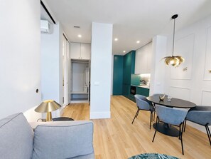 Un salon moderne avec un canapé, une table à manger et des chaises, ainsi qu’un coin cuisine doté de meubles de couleur turquoise.